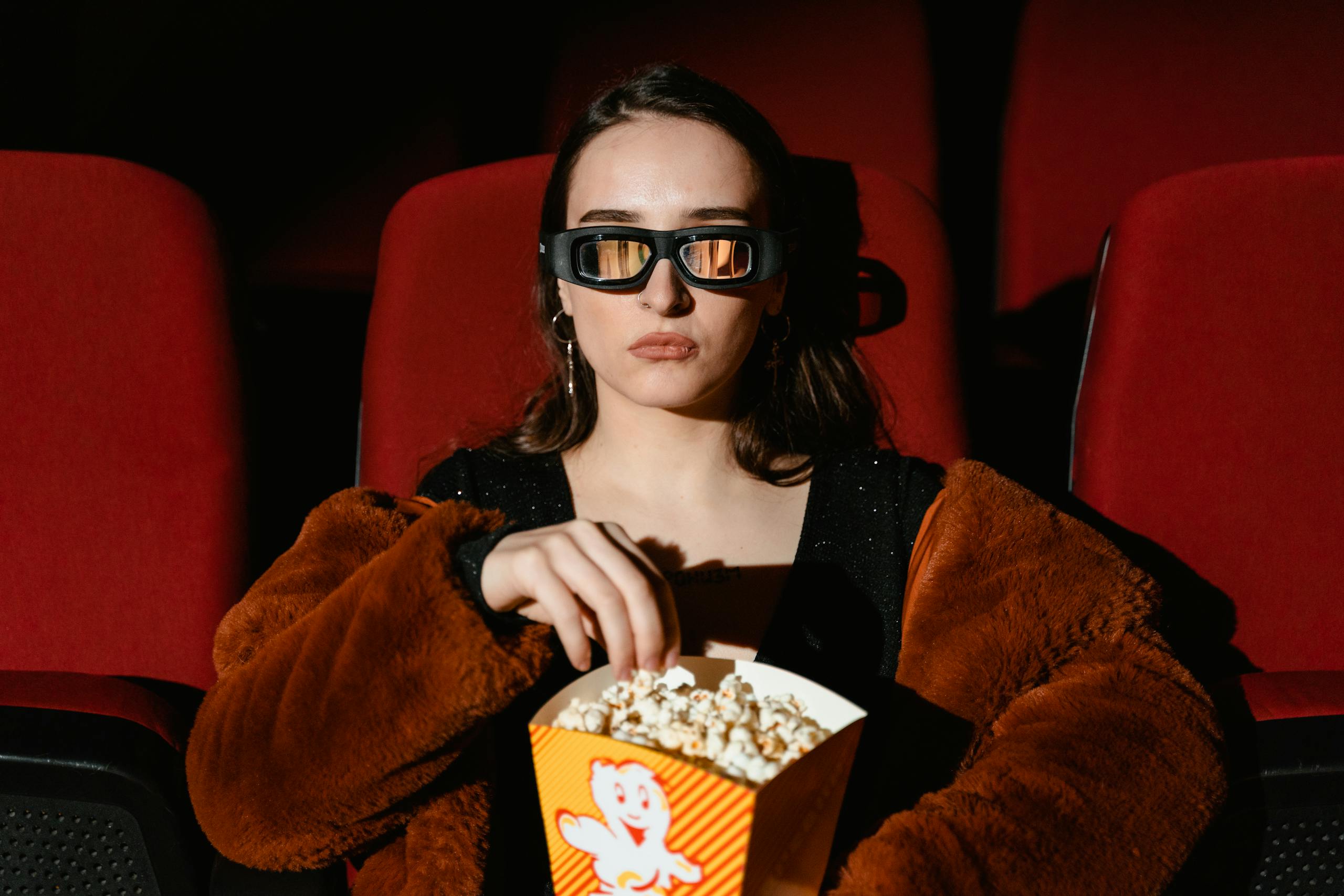 A woman in a fur coat enjoying popcorn while watching a 3D movie in a cinema.