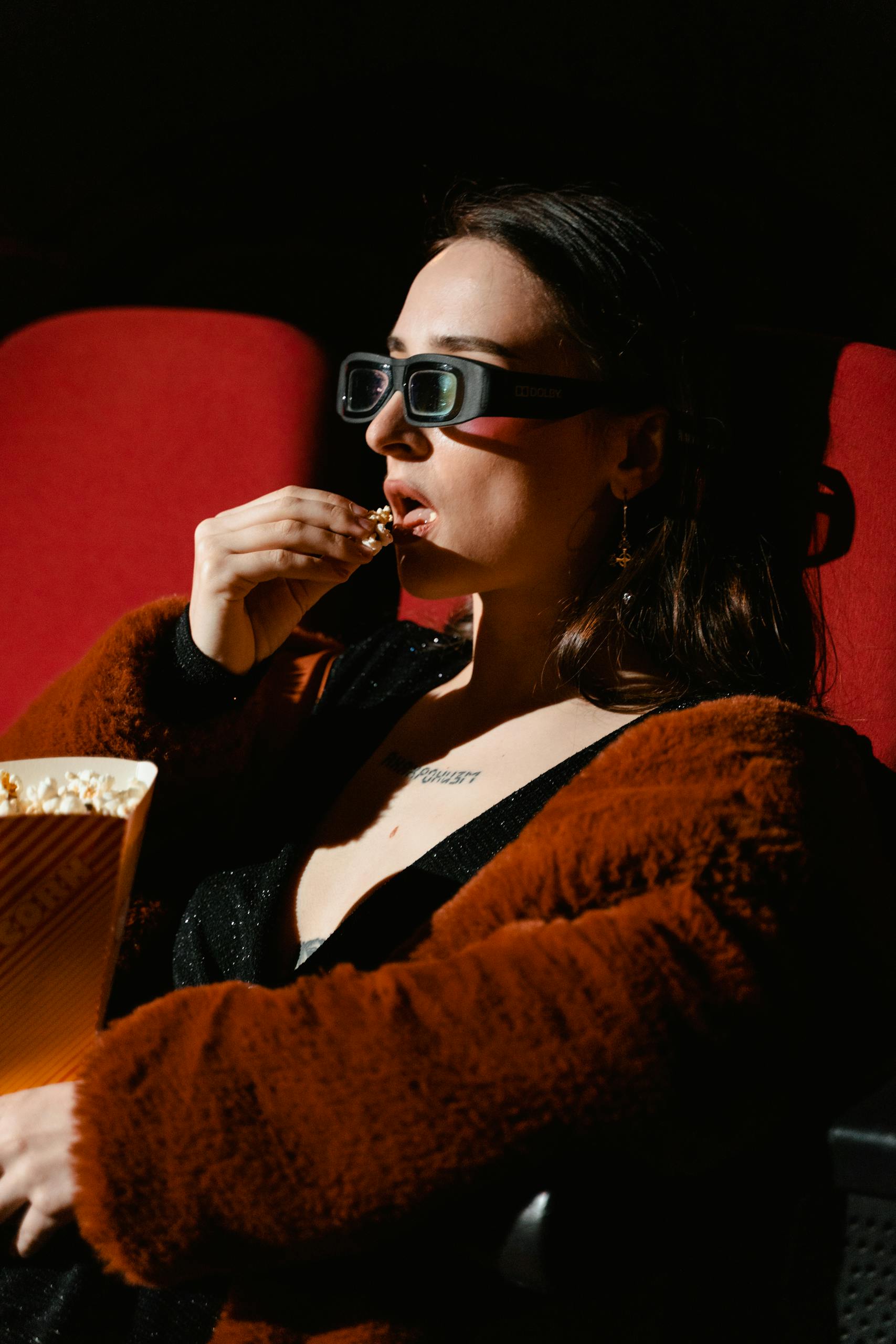 Woman in a cinema seat enjoying popcorn while watching a film.